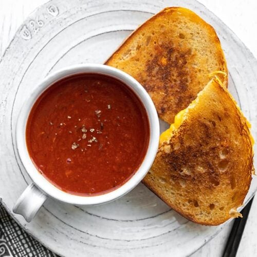 Tomato herb soup in a mug on a plate with grilled cheese