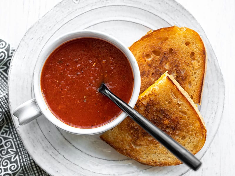 Overhead view of a mug full of tomato soup with a black spoon in the center