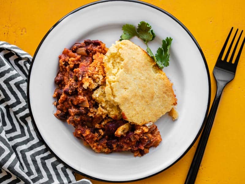 A plate with one serving of Chili Cornbread Skillet on a yellow surface with striped napkin