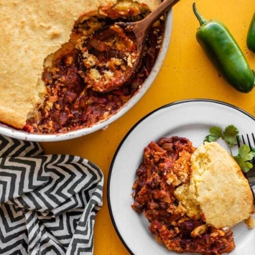 Chili cornbread skillet with some scooped out onto a white plate beside the skillet