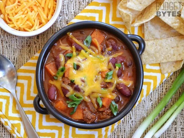 Top view of a bowl of Chorizo Sweet Potato Chili with a spoon and small bowl of shredded cheese on the side 