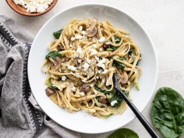 A shallow bowl full of Spinach and Artichoke One Pot Pasta with spinach and feta on the sides.