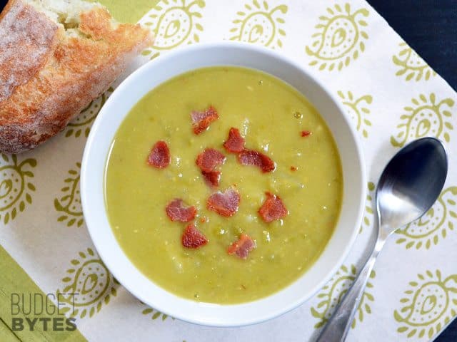 A bowl of split pea and potato soup with bacon served with bread.