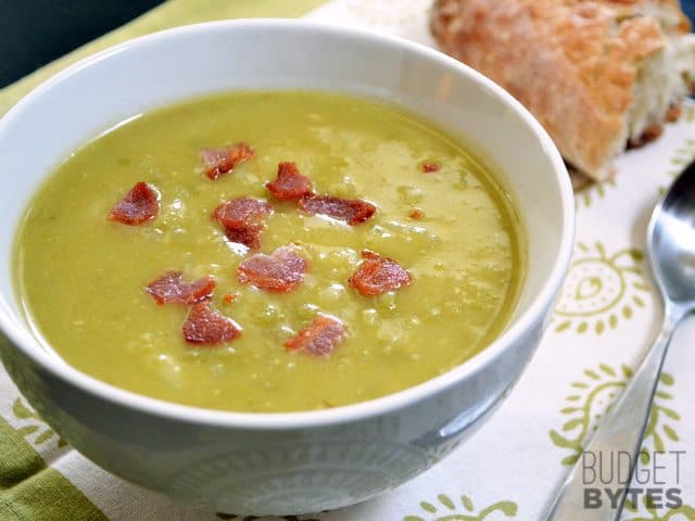 Side view of a bowl of Split Pea Bacon & Potato Soup with spoon and a piece of bread on the side 