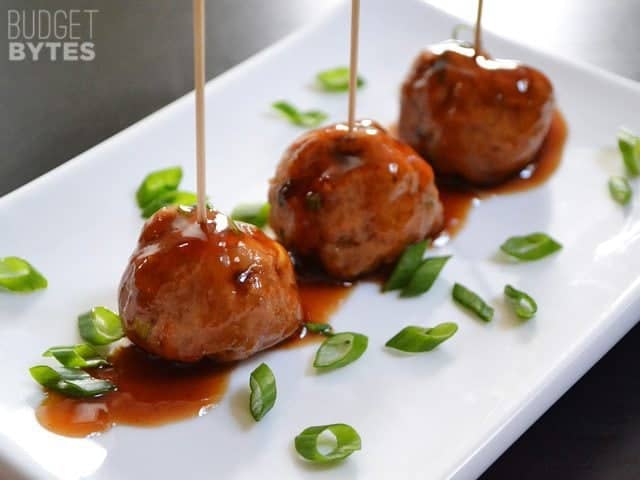 Three Turkey Sriracha Meatballs with toothpicks plated on a square plate and garnished with green onions 