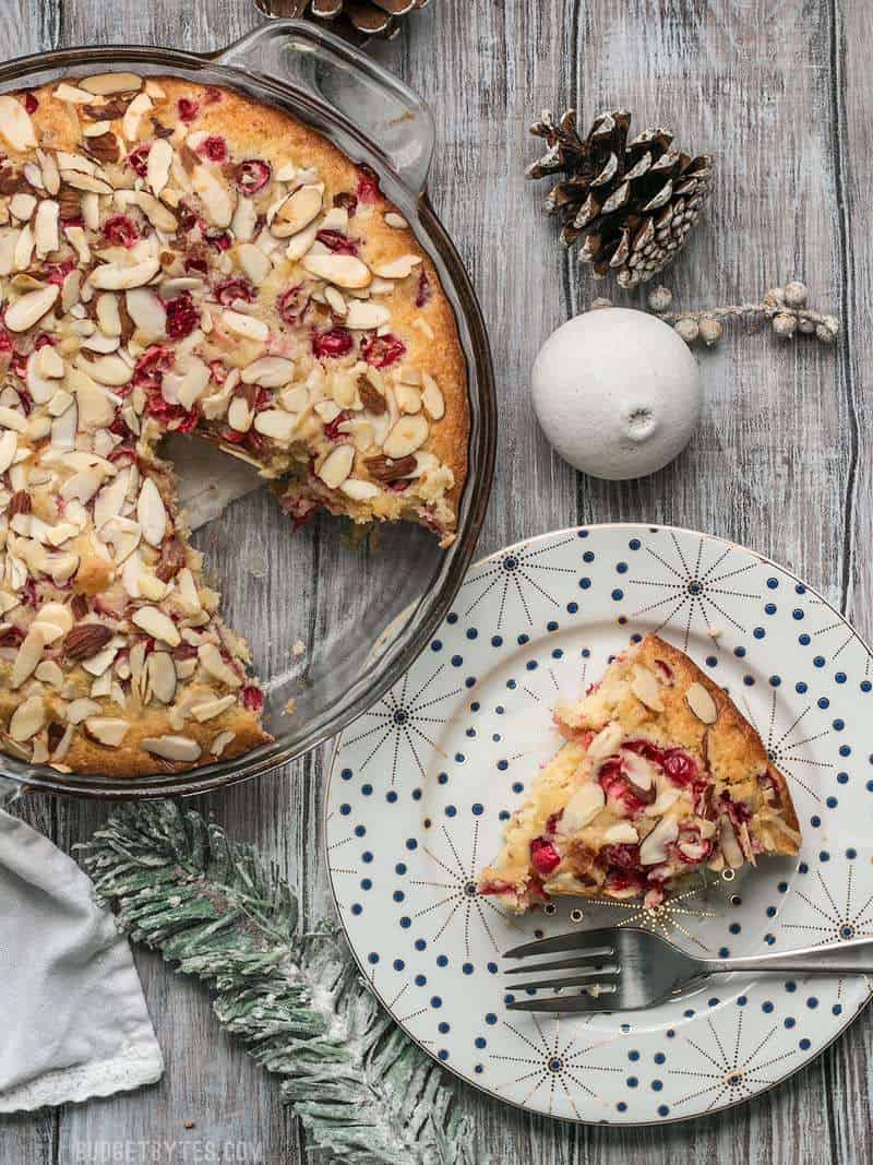 Top view of a full Cranberry Almond Cake with a slice taken out and plated on plate with fork 