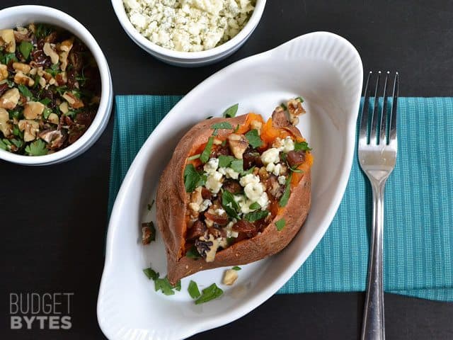 Top view of finished Date & Gorgonzola Stuffed Sweet Potato in a dish with a bowl of extra toppings on the side, as well as a fork 