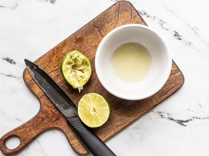 A lime cut in half, one half has been squeezed, next to a bowl with lime juice.