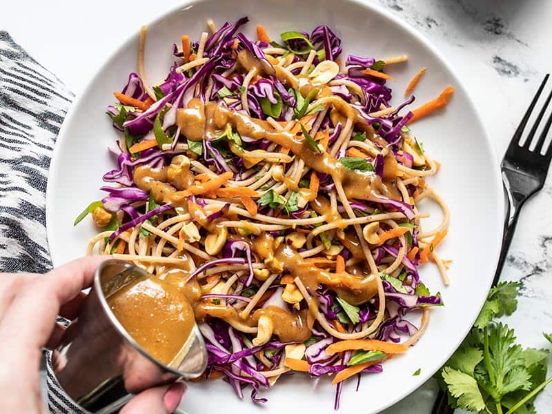 peanut lime dressing being poured over a colorful cabbage salad.