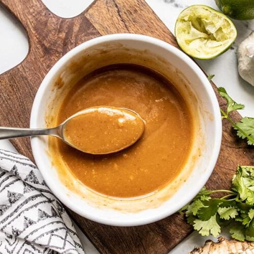 A spoon lifting some peanut lime dressing out of a bow, squeezed lime and cilantro on the side.