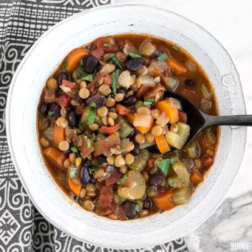 A spoon in a bowl of chunky lentil and vegetable soup.