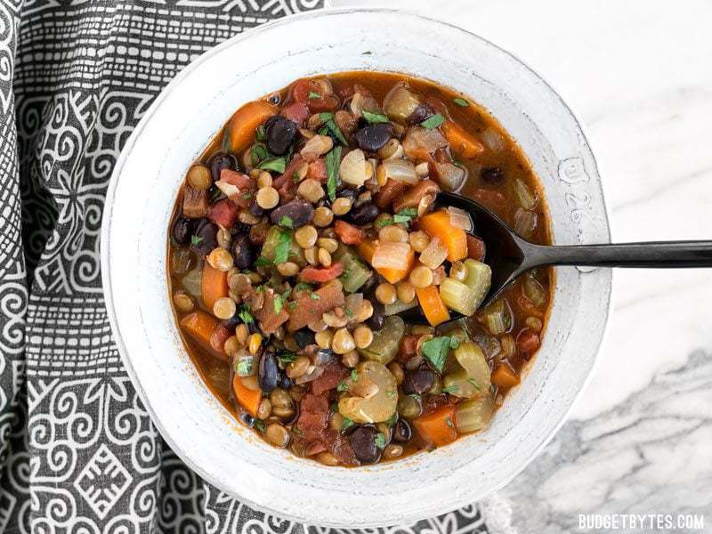 A spoon in a bowl of chunky lentil and vegetable soup.