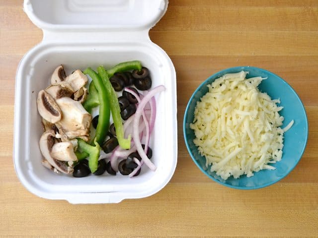 Toppings in take out container with a bowl of shredded cheese next to it 