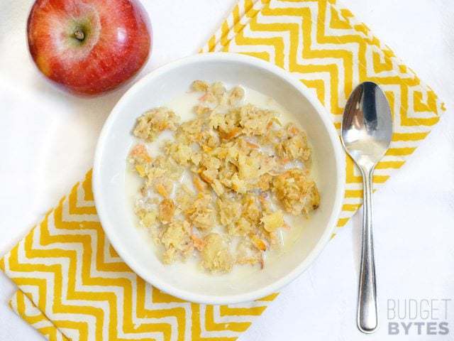 Top view of a bowl of Morning Glory Baked Oatmeal on a yellow chevron napkin, spoon and apple on the side 