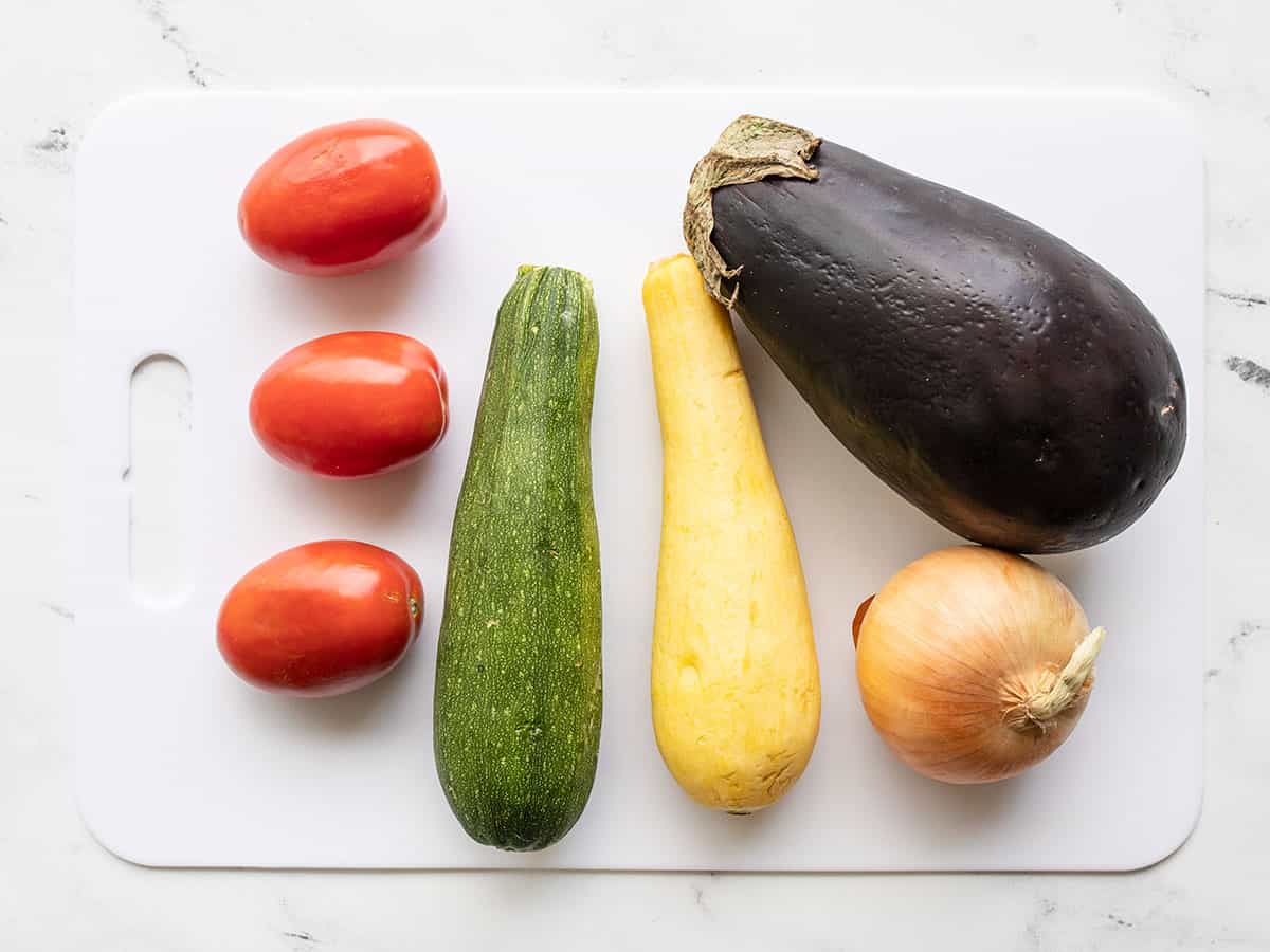 Eggplant, onion, squash, and tomatoes whole on a cutting board