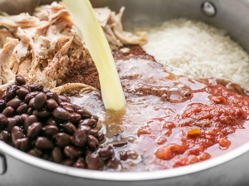 Chicken broth being poured into skillet with other ingredients 