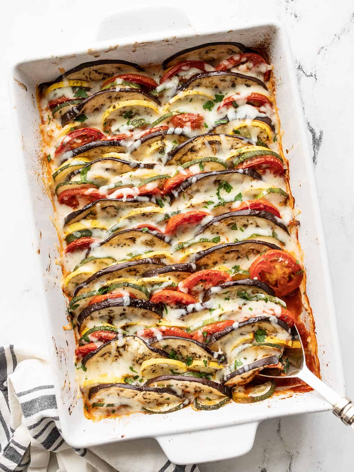 Overhead view of oven roasted ratatouille in the casserole dish with a serving spoon