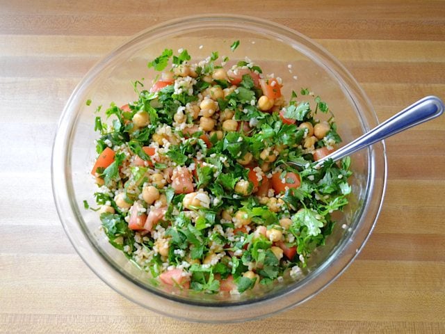 Salad ingredients mixed together in mixing bowl with spoon 