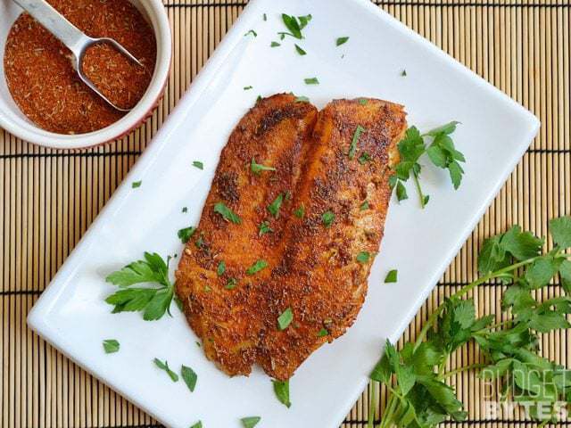 Top view of a plate of Blackened Tilapia garnished with parsley, a bowl of seasoning on the side 