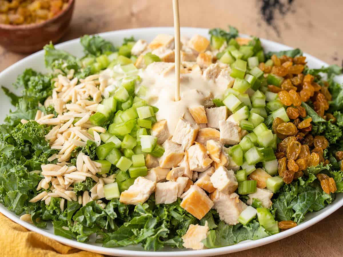 Side view of dressing being poured onto kale and chicken salad