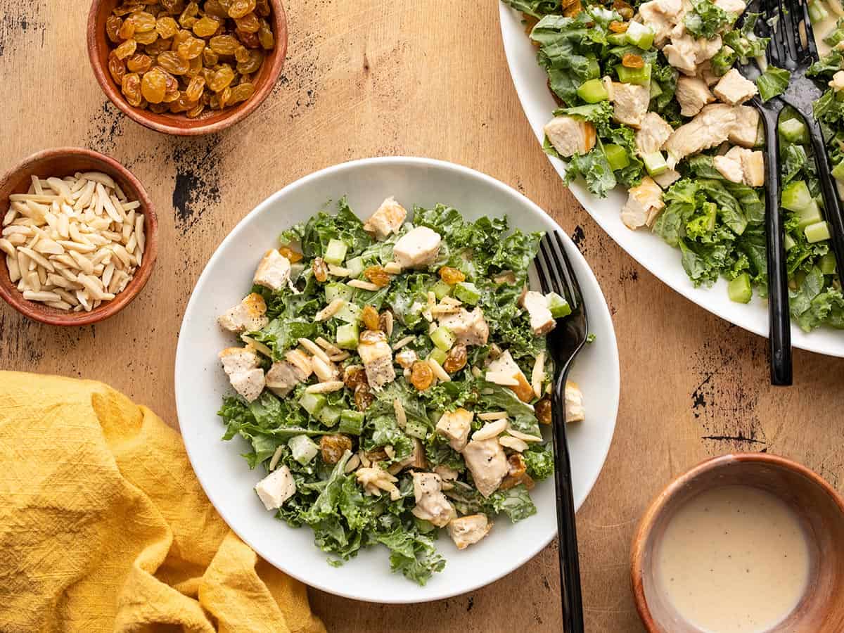 Tossed kale and chicken salad in a bowl next to the serving platter full of kale salad