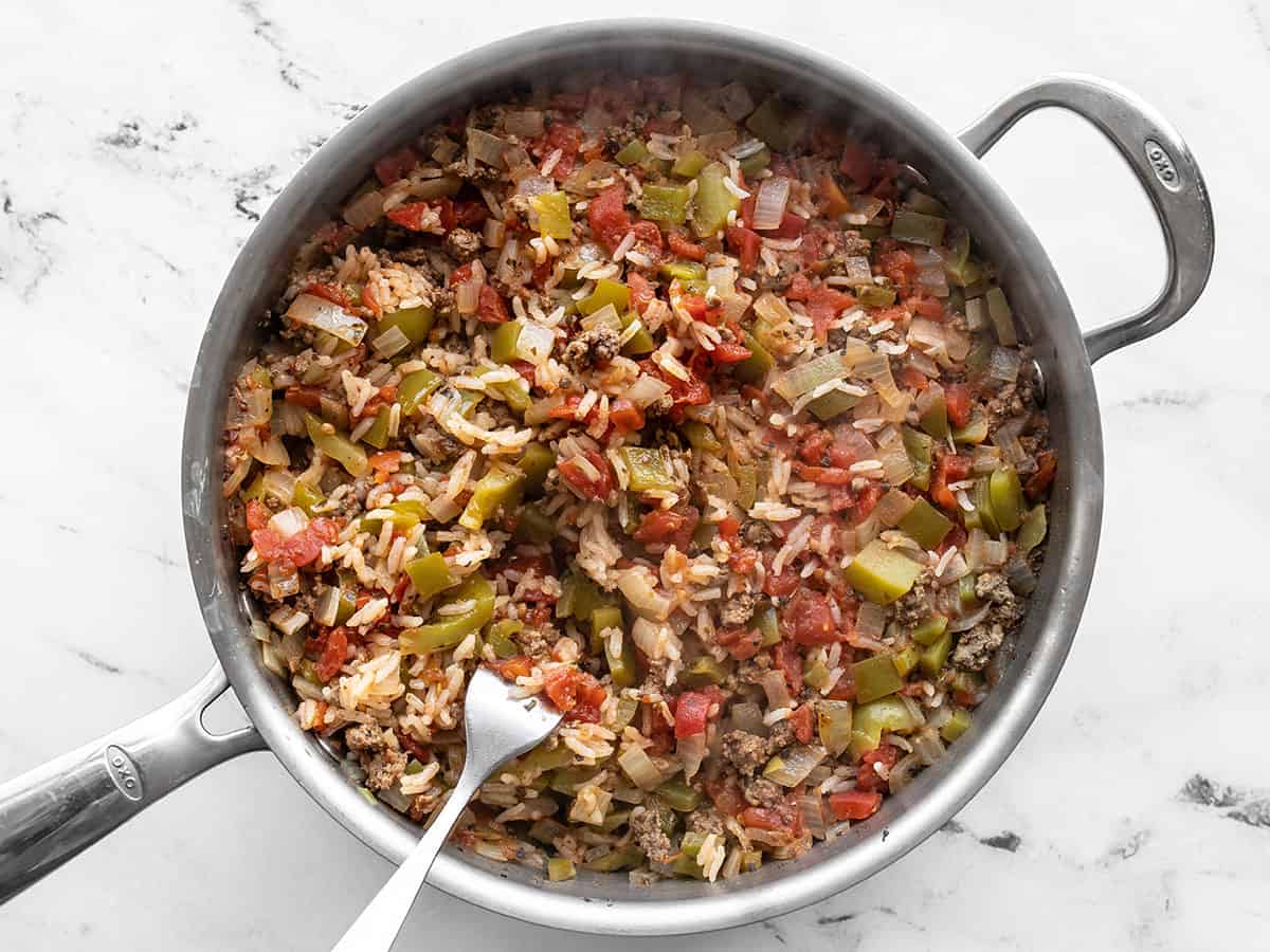 Rice being fluffed with a fork in the skillet