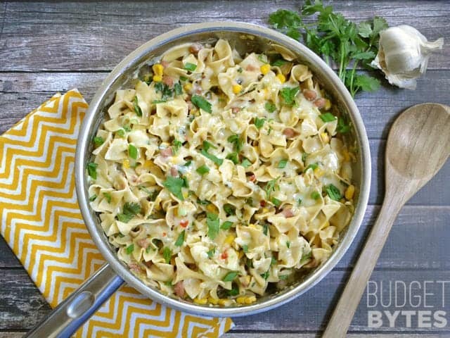 Top view of a skillet of cooked Creamy Vegetarian Enchilada Pasta, wooden spoon and a yellow chevron napkin on the side 