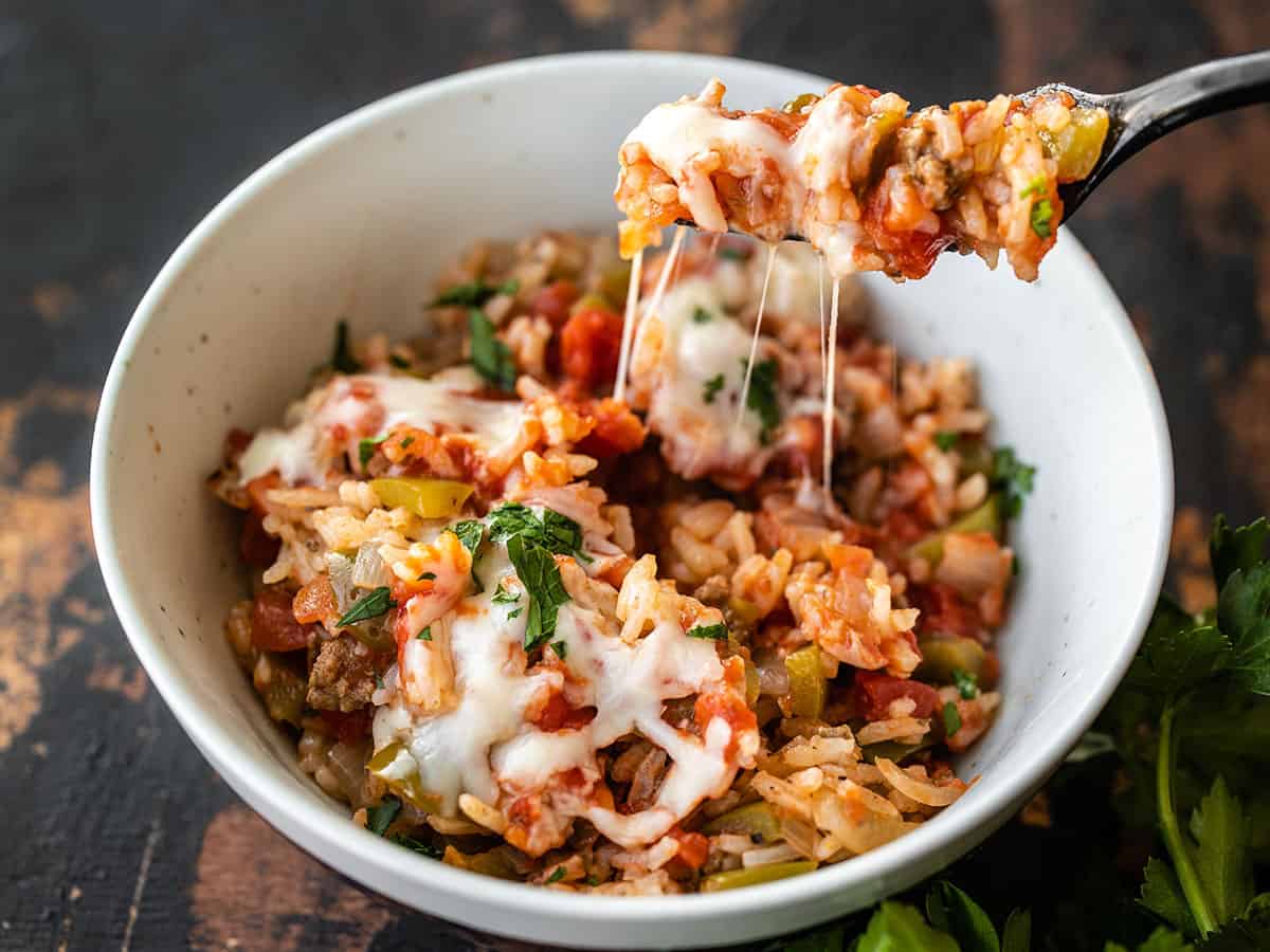 A fork lifting some rice and cheese from a bowl of unstuffed bell peppers