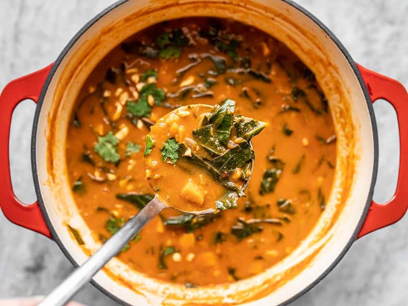 A ladleful of Vegan Peanut Stew with the full pot in the background