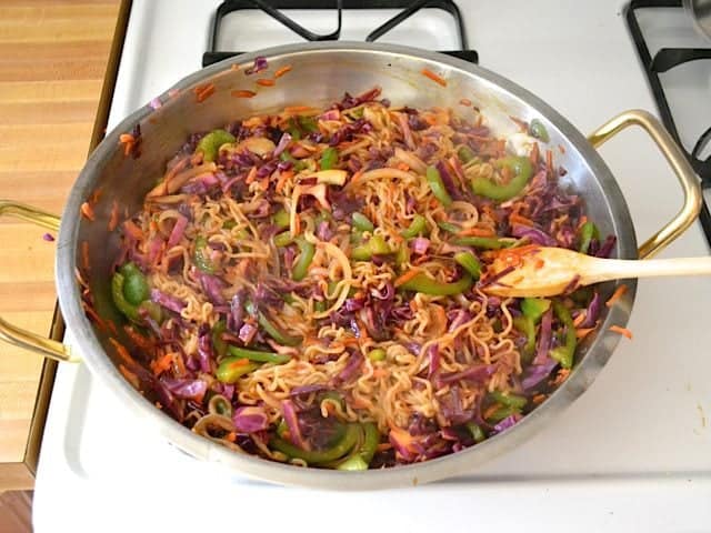 Cooked ramen added to veggies and sauce in skillet on stove top 