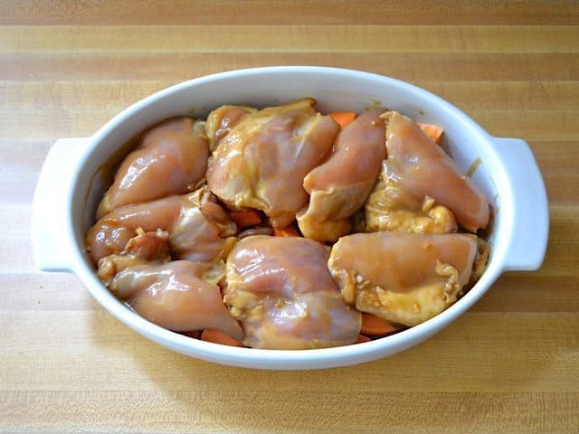 Marinated raw Chicken Thighs placed over cubed sweet potatoes in casserole dish 