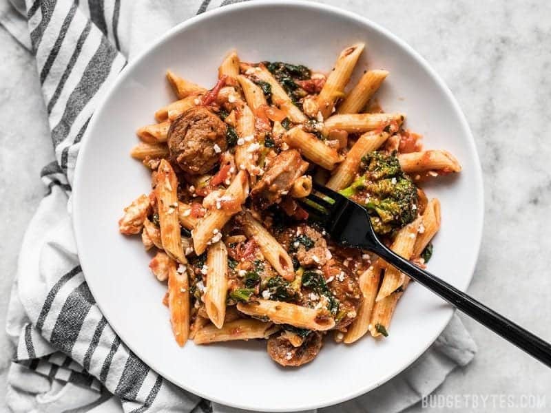 A plate full of Penne Pasta with sausage and greens, a black fork in the center