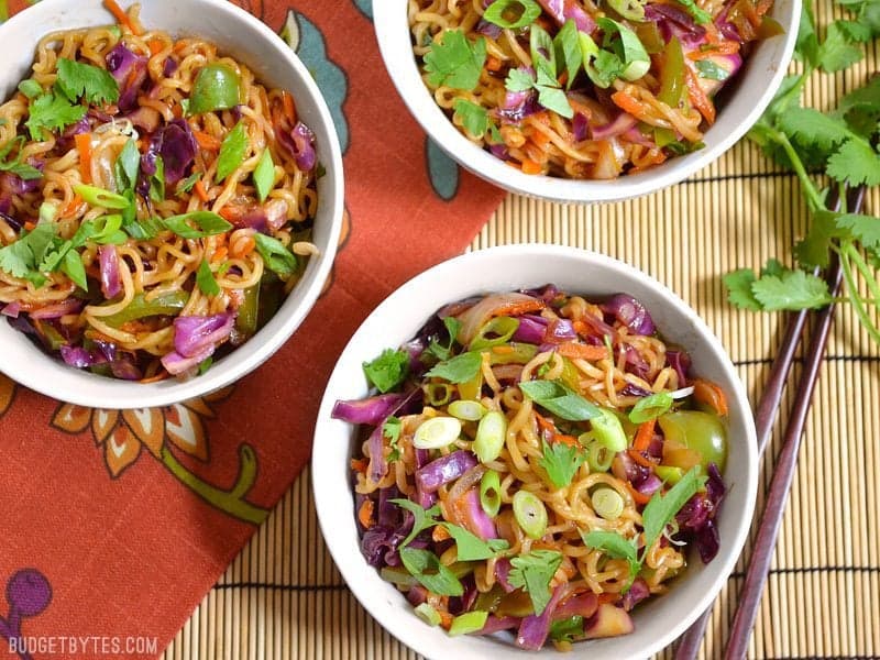 Top view of three bowls of vegetable stir fry with noodles with chop sticks on the side 