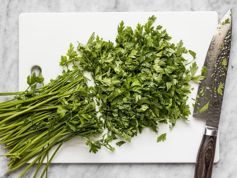 Chopping parsley on cutting board with large knife 