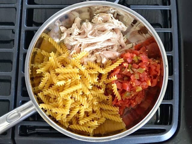 Rotel, dry pasta and shredded chicken in skillet on stove top 