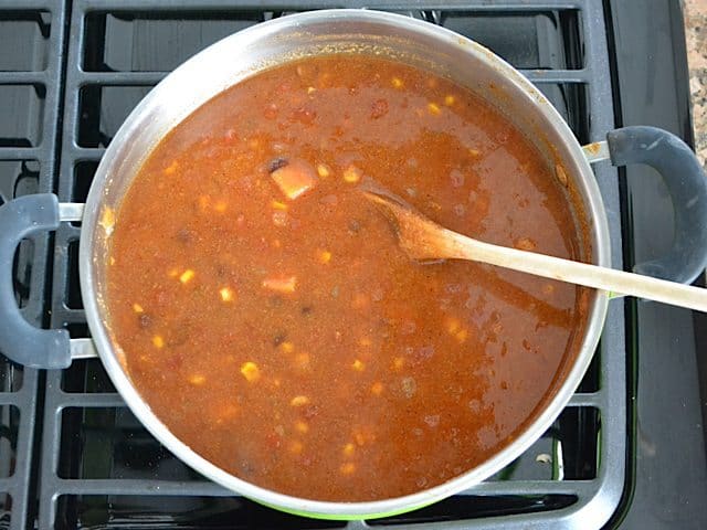 Tortilla Soup simmering in pot on stove top, stirred with wooden spoon 