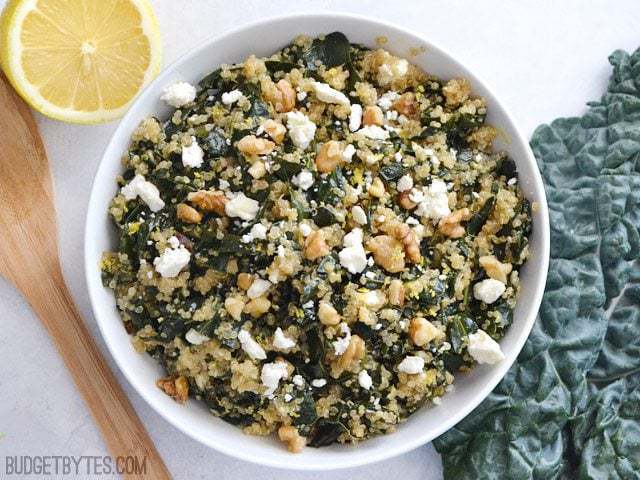 Top view of a bowl of Lemony Kale and Quinoa Salad with a wooden spoon and a half a lemon on the side 