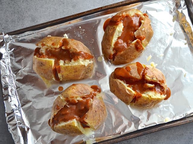 Potatoes cut open with enchilada sauce poured on top of each 