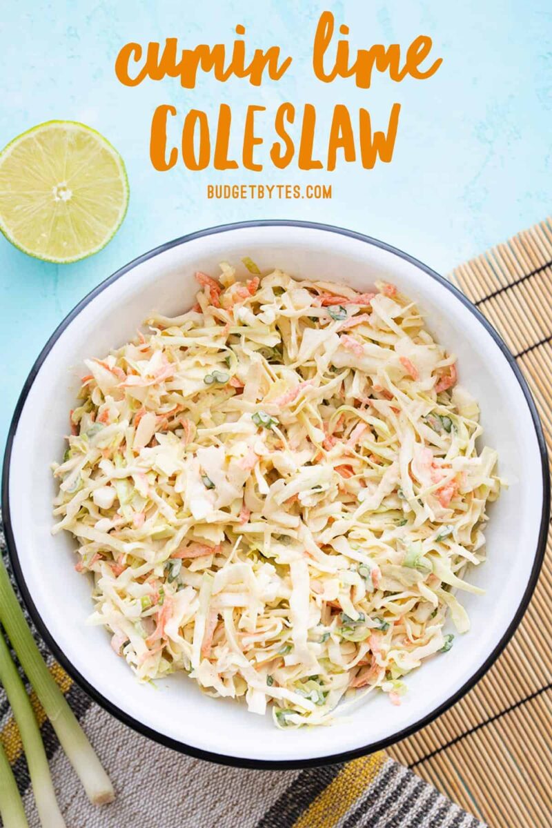 Overhead view of a bowl of cumin lime coleslaw with limes and green onion on the side