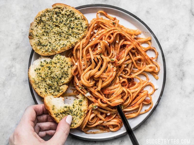 Two slices of homemade freezer garlic bread on a plate with pasta and red sauce