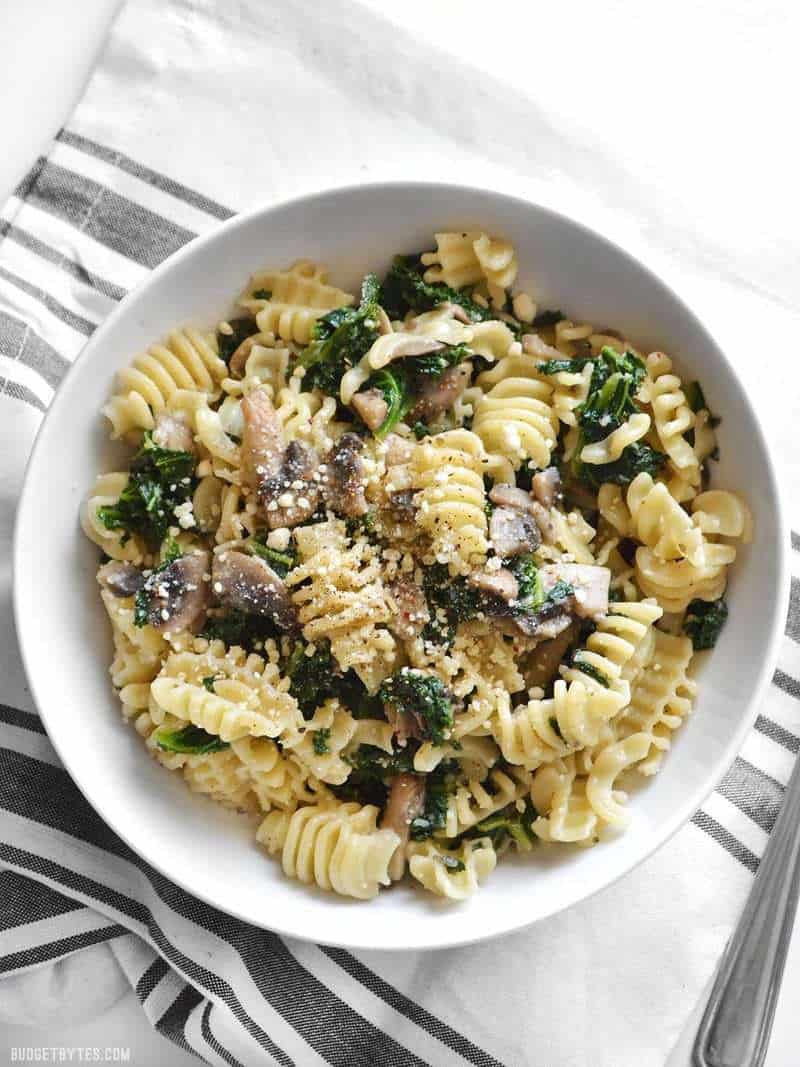 Top view of a bowl of Parmesan & Pepper Kale Pasta sitting on a gray and white stripped napkin 