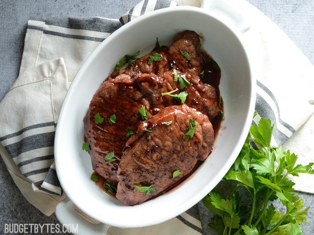 Top view of a dish of Blackberry Sage Pork Chops sitting on a gray and white napkin with a sprig of cilantro on the side 