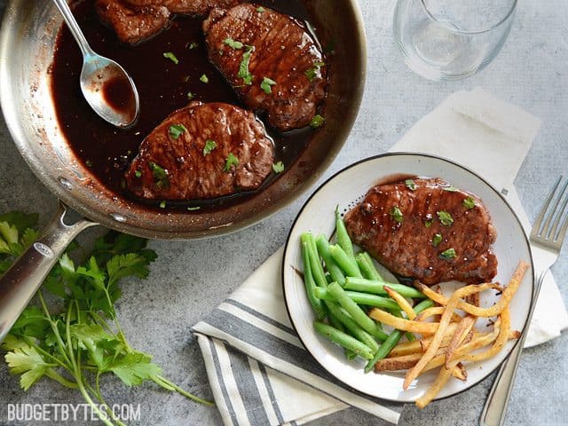 Pan of Blackberry Sage Pork Chops with a plate with one pork chop, green beans and fries on the side 