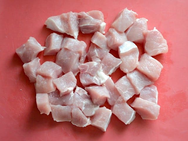 Pork chops cut into chunks on a red cutting board