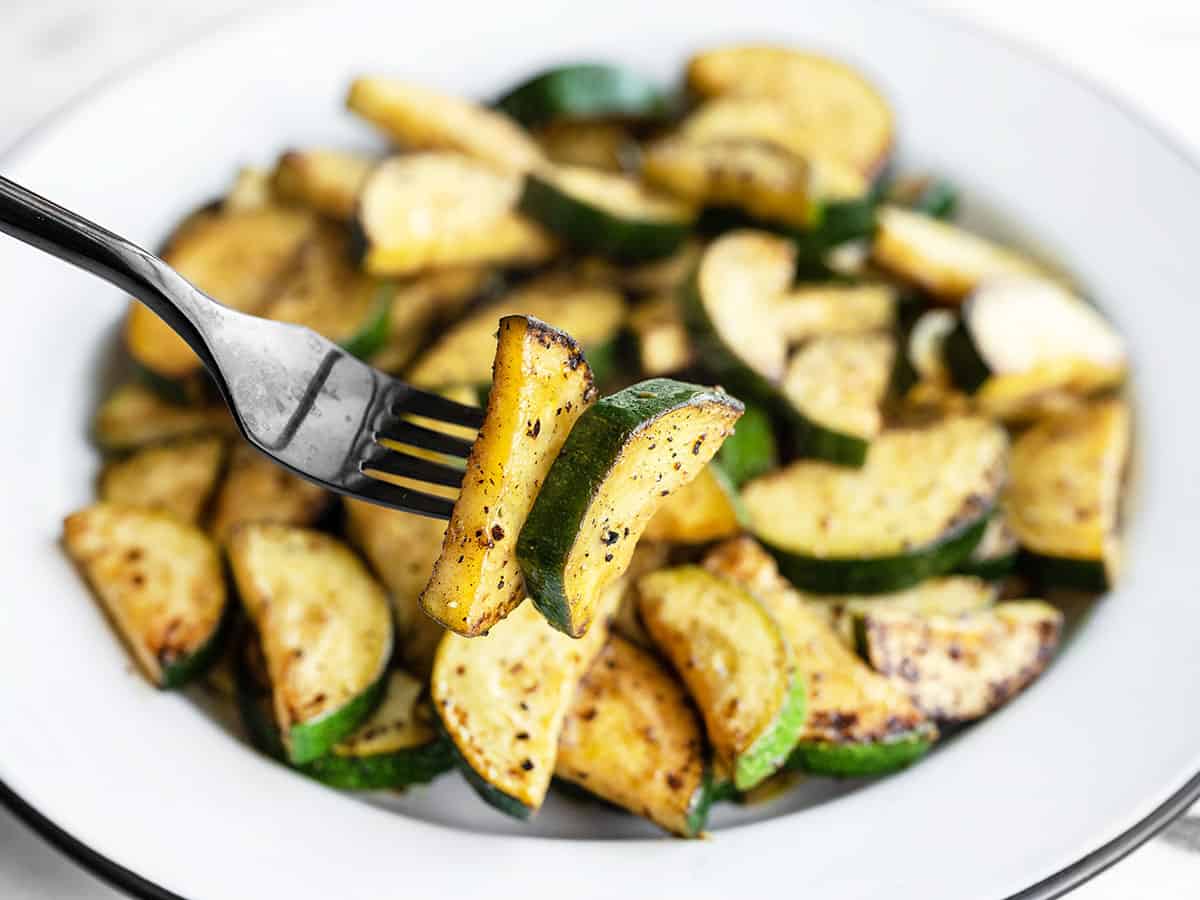 Close up of a forkful of lemon pepper zucchini with the bowl in the background