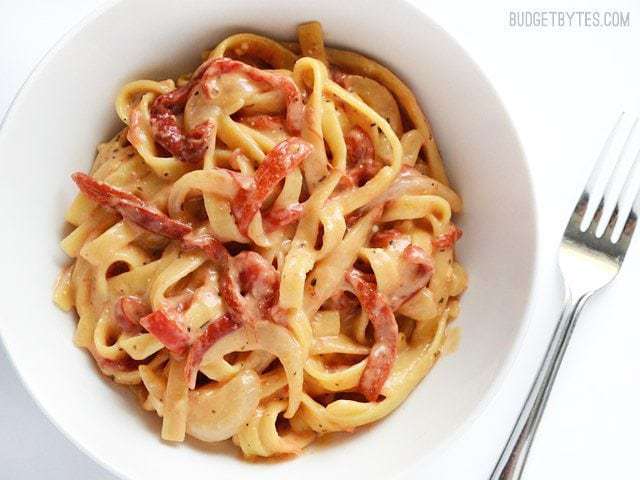 A close-up of pasta with roasted red peppers and herbs with a fork.