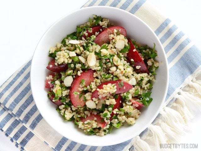 A colorful plum salad garnished with nuts and herbs.