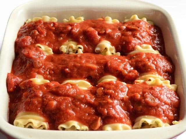 Sauce poured over vegetable lasagna roll ups in the casserole dish