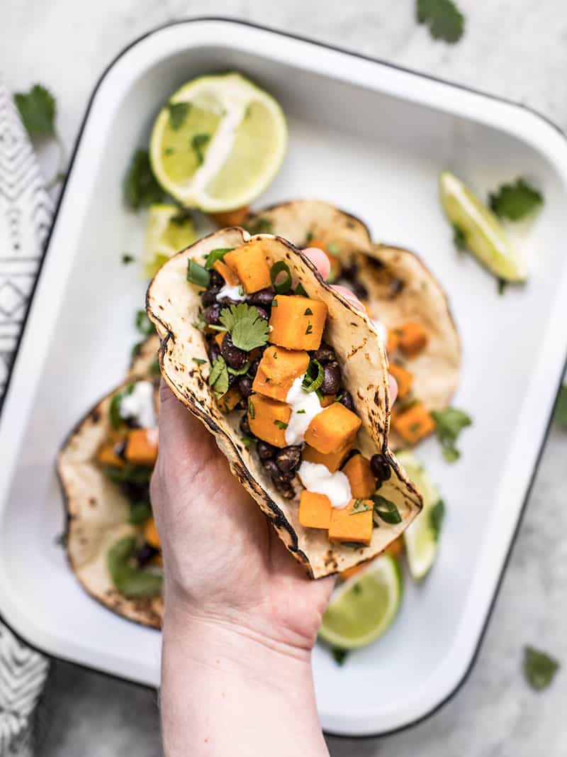 A hand holding a sweet potato taco close to the camera