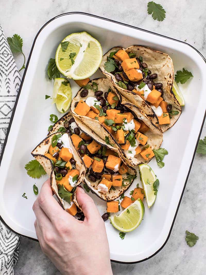 A hand picking up a sweet potato taco out of the serving dish